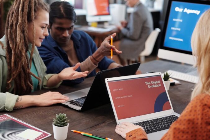Three diverse marketing agency team members collaborating around laptops showing digital evolution presentation in modern off
